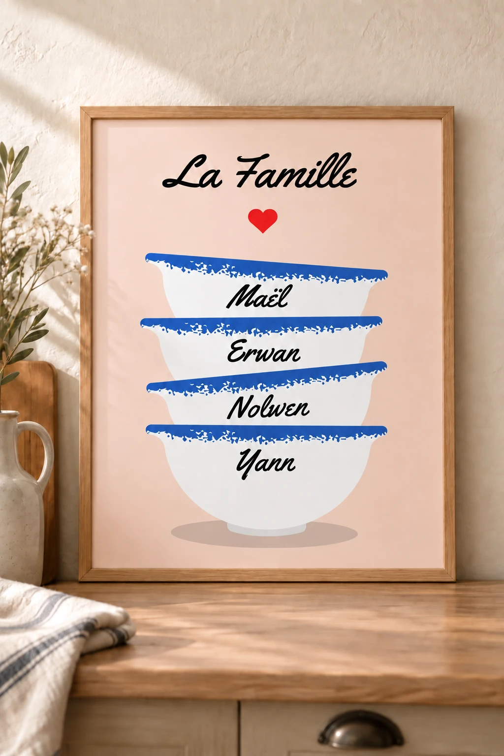 Affiche personnalisée La Famille avec quatre bols bretons blancs et bleus portant des prénoms, un cœur rouge et un fond rose poudré, mise en scène dans un cadre bois